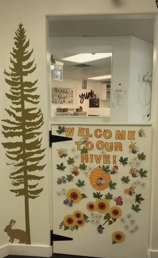 A classroom door decorated with paper sunflowers and a painted pine tree on the wall